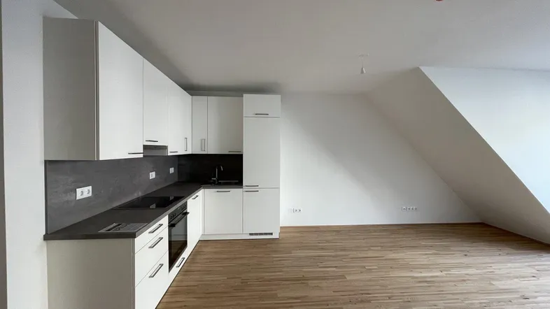 Moderne Einbauküche mit weißen Schränken und Holzboden in einem offenen Wohnbereich.
