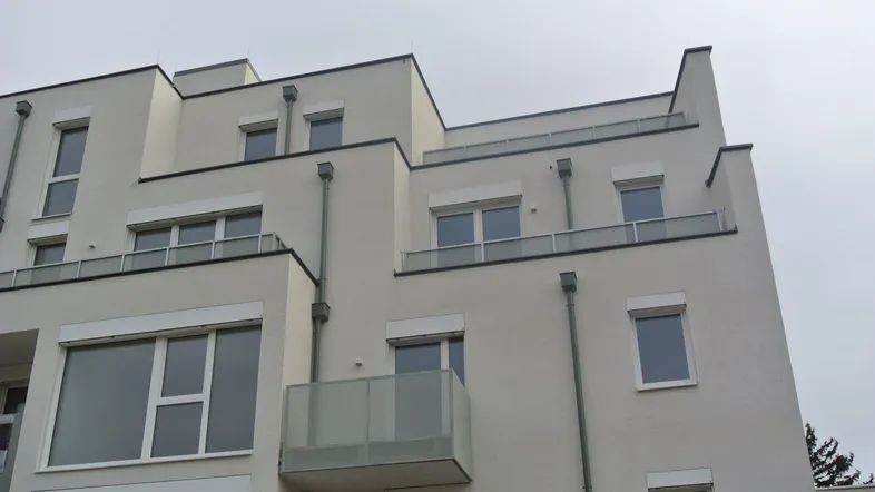 Moderne Wohnhausfassade mit mehreren Balkonen und großen Fenstern unter bewölktem Himmel.