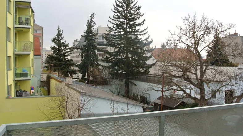 Blick von einem Balkon auf die umliegenden Gebäude und Bäume in einer städtischen Umgebung.