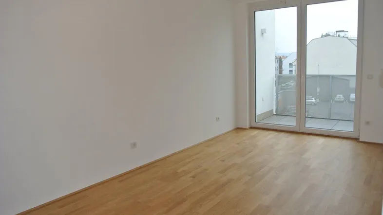 Helles Zimmer mit Holzboden und großen Fenstertüren, die zu einem Balkon führen.