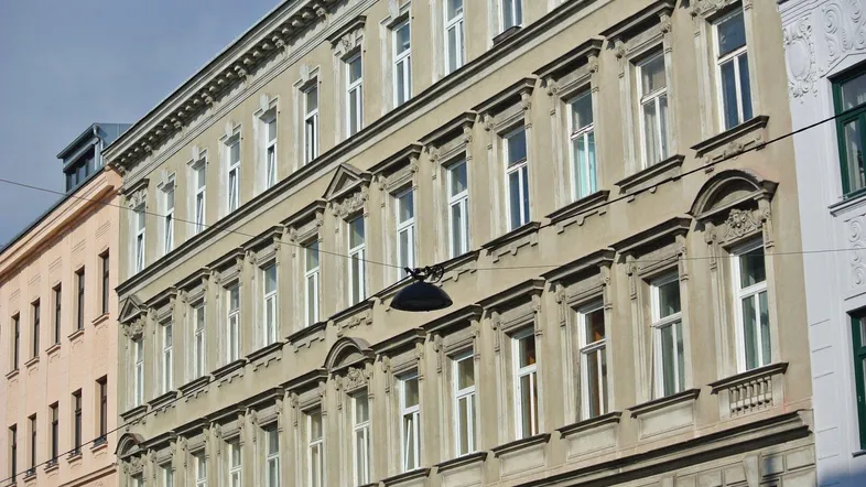 Historische Fassade eines Altbaus mit vielen Fenstern und dekorativen Elementen unter blauem Himmel.