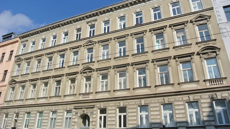 Klassisches Wiener Zinshaus mit historischer Fassade und vielen Fenstern unter blauem Himmel.