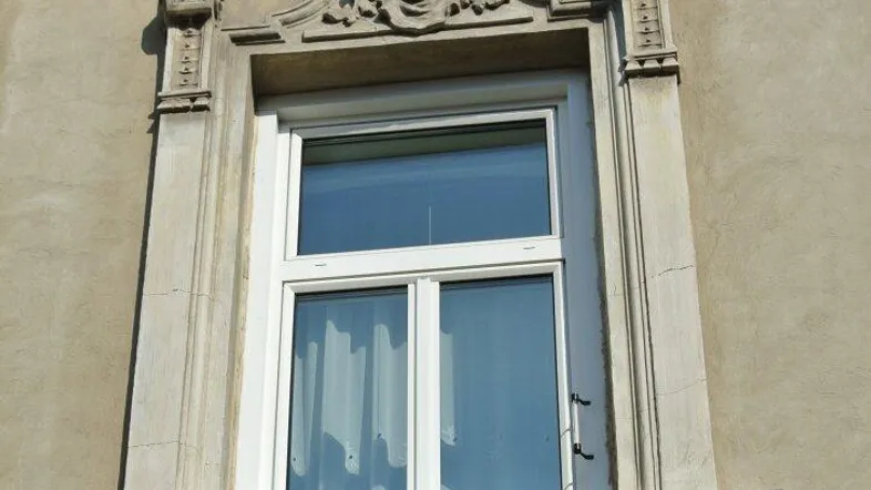 Detailansicht eines Fensters mit aufwendigen Stuckverzierungen und Balustrade an einer historischen Fassade.