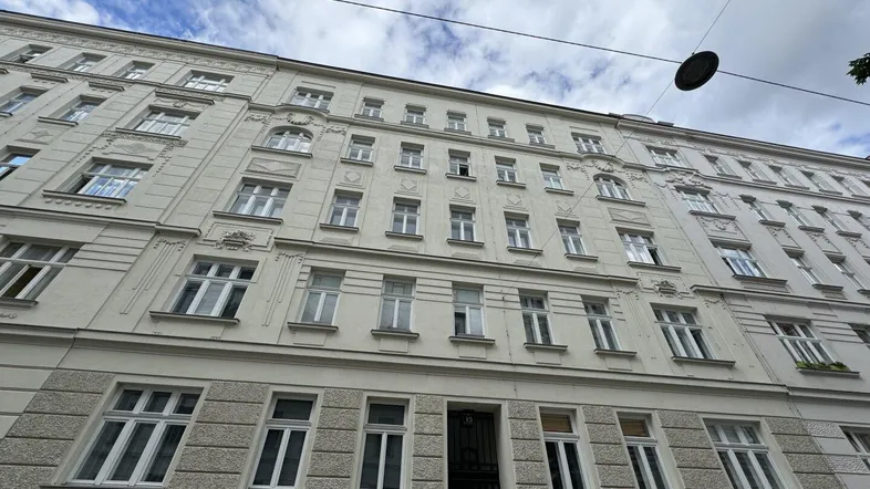 Mehrstöckiges Altbaugebäude mit klassischer Fassade und zahlreichen Fenstern unter bewölktem Himmel.