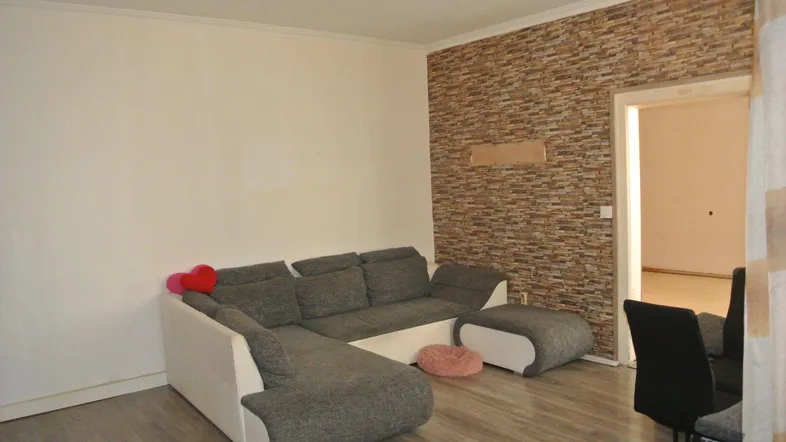 Modernes Wohnzimmer mit Ecksofa, Holzboden und einer Wand mit Steinoptik.