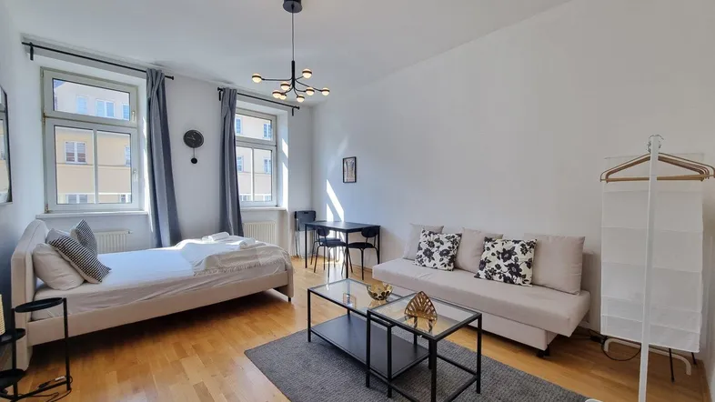 Helles Studio-Apartment mit Holzboden, Schlafbereich, Sofa und Esstisch in modernem Stil.