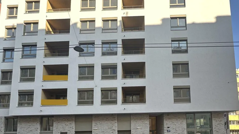 Modernes Mehrfamilienhaus mit mehreren Balkonen und Geschäften im Erdgeschoss in städtischer Umgebung.