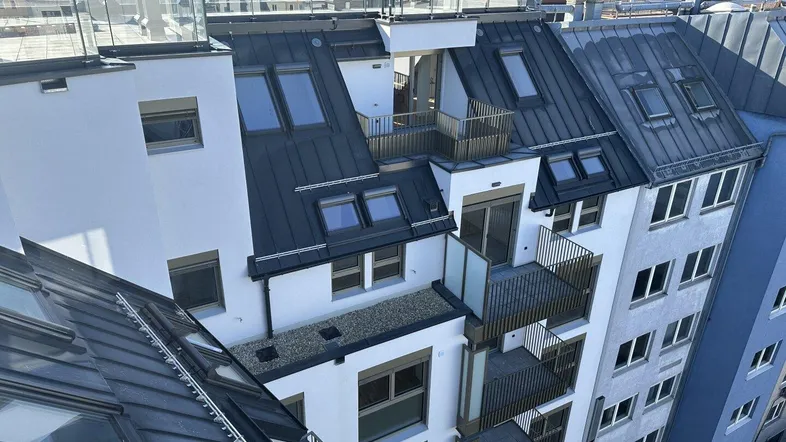 Moderne Dachgeschosswohnungen mit Balkonen und großen Fenstern in einem städtischen Gebäude.