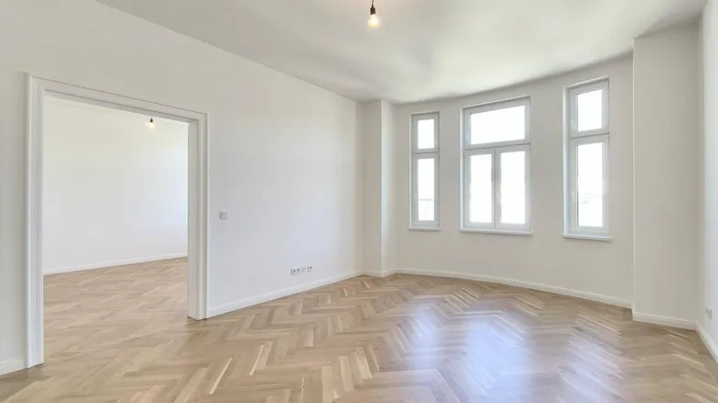 Helles Zimmer mit Fischgrätparkett und hohen Fenstern, bereit zur Einrichtung.