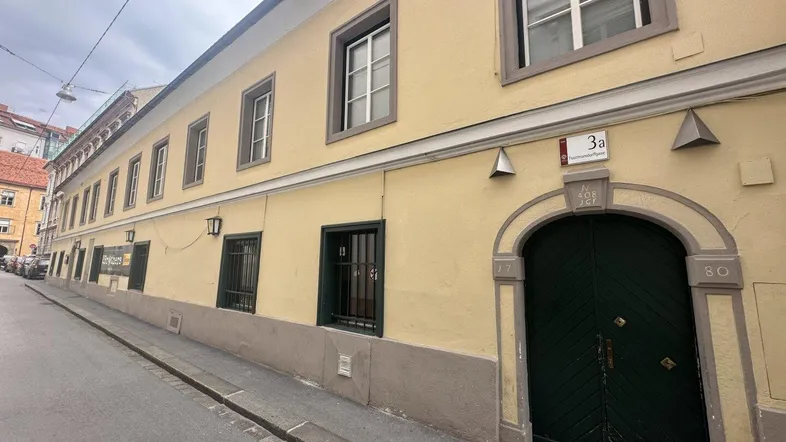 Gelbe Fassade eines Altbaus mit dunklem Holztor und Fenstern zur Straße.