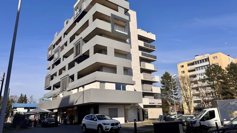 Modernes Mehrfamilienhaus mit gestuften Balkonen und Geschäften im Erdgeschoss.