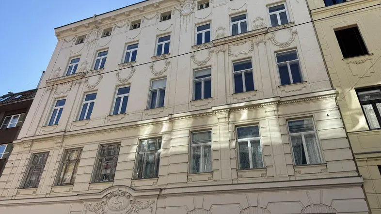 Historische Fassade eines Wohngebäudes mit mehreren Stockwerken und klassischen Verzierungen unter blauem Himmel.