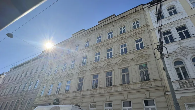 Historische Fassade eines Altbaus mit reich verzierten Details unter strahlendem Sonnenschein.