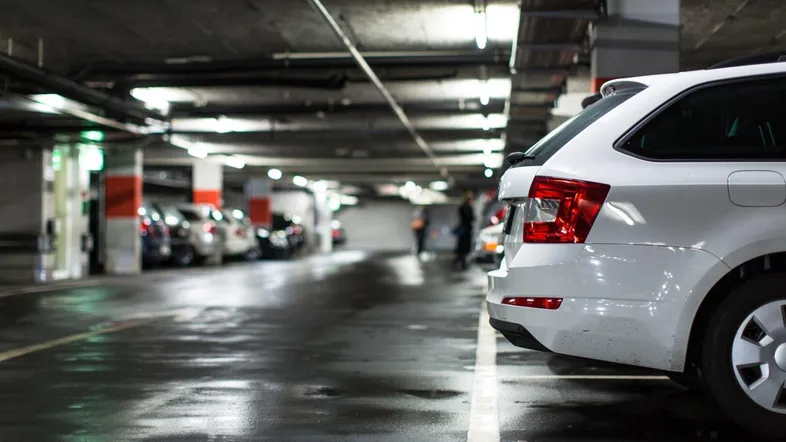 Tiefgarage mit mehreren geparkten Fahrzeugen und nassen Böden unter künstlicher Beleuchtung.