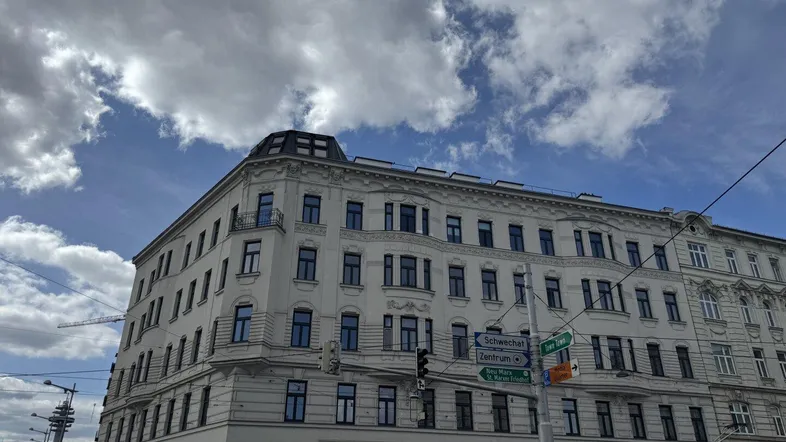 Historisches Eckgebäude mit klassischer Architektur und vielen Fenstern unter bewölktem Himmel.