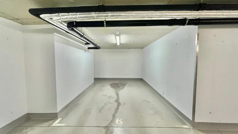 Leerer Tiefgaragenstellplatz mit Betonboden und sichtbaren Leitungen an der Decke.