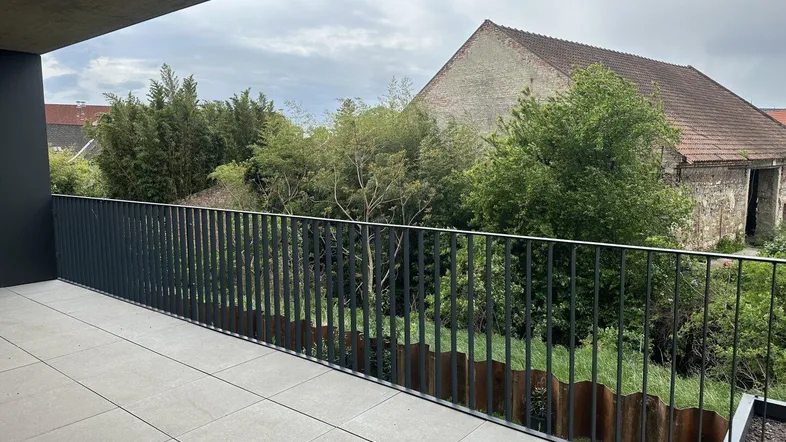Moderner Balkon mit Fliesenboden und Blick ins Grüne sowie auf ein historisches Gebäude.