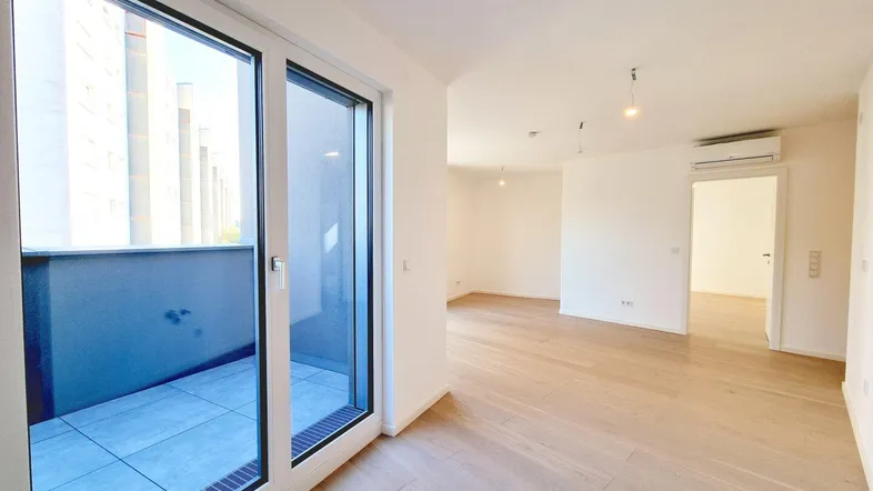Helles Zimmer mit Holzboden und Zugang zu einem gefliesten Balkon, ausgestattet mit Klimaanlage.