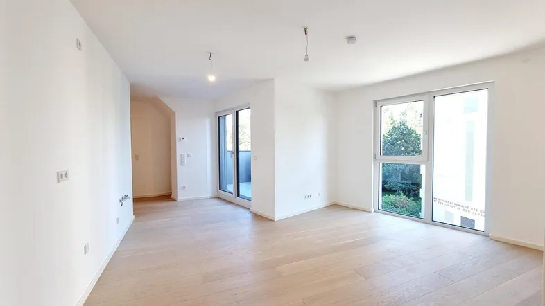 Helles, leeres Zimmer mit Holzboden und Zugang zu einem Balkon, ideal als Wohnbereich.