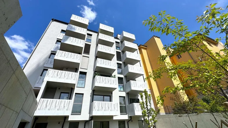 Modernes Mehrfamilienhaus mit vielen Balkonen und weißer Fassade unter blauem Himmel.