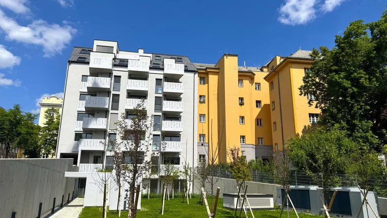 Modernes Wohngebäude mit weißer Fassade und begrüntem Außenbereich unter blauem Himmel.