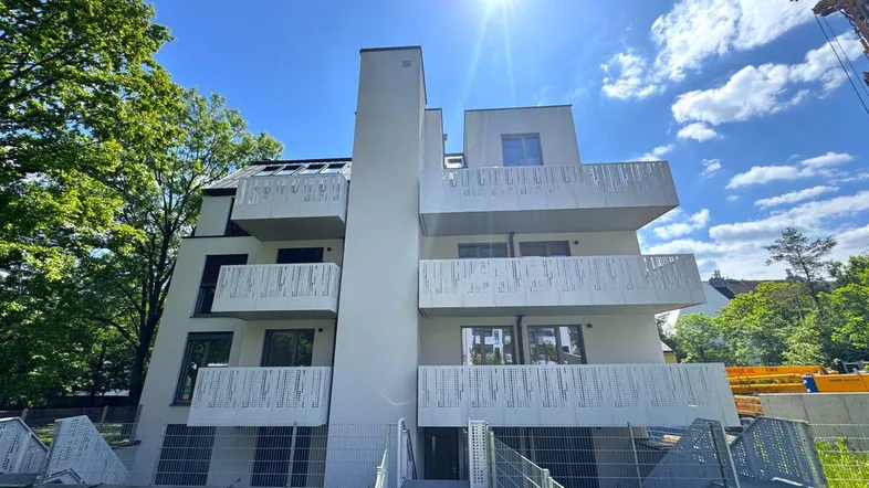Modernes Apartmentgebäude mit mehreren Balkonen und zeitgenössischer Architektur unter strahlendem Himmel.