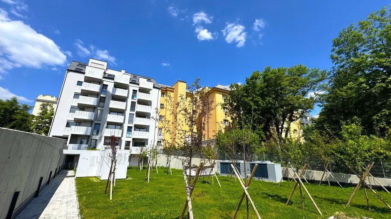 Modernes Wohngebäude mit weißer Fassade und Balkonen, umgeben von einer grünen Außenanlage.
