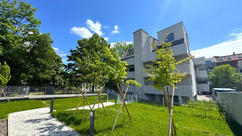 Modernes Mehrfamilienhaus mit gepflegter Grünanlage und junger Bepflanzung unter blauem Himmel.