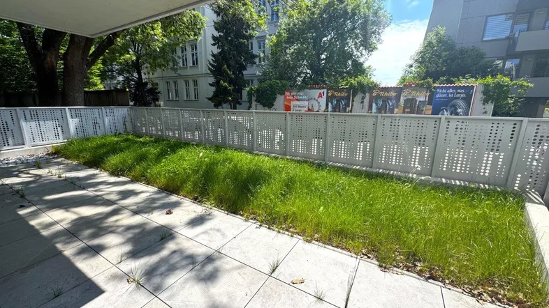 Gepflasterte Terrasse mit angrenzender Rasenfläche und Blick auf Bäume und Gebäude.