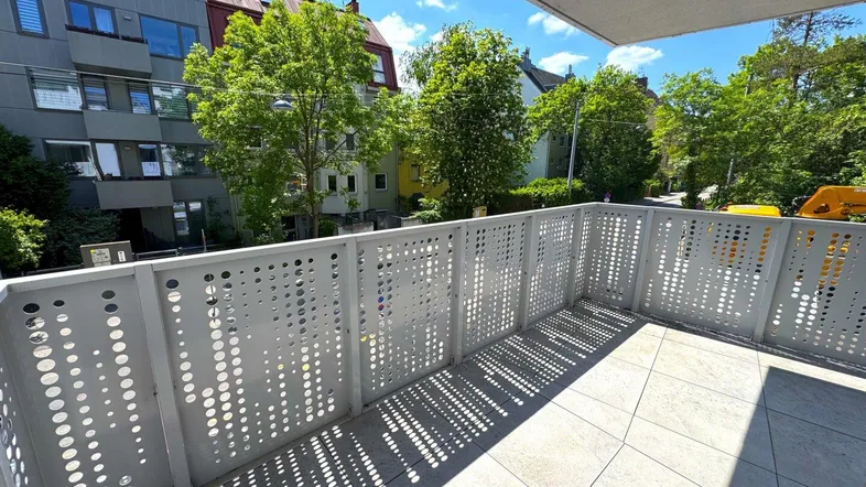 Heller Balkon mit modernem Lochblechgeländer und Blick auf die umliegenden Gebäude und Bäume.