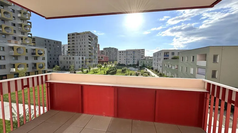 Heller Balkon mit rotem Geländer und weitem Blick auf moderne Wohngebäude und Grünflächen.