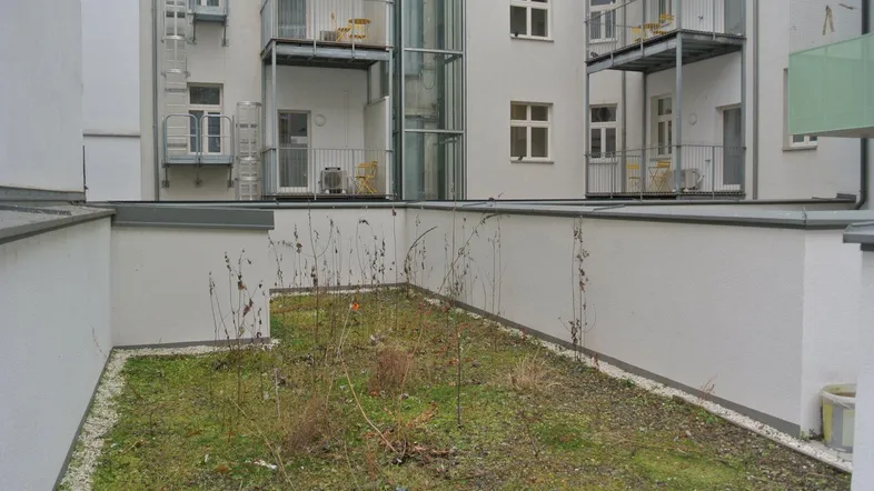 Kleiner, begrünter Innenhof mit Blick auf die umliegenden Balkone und einen externen Aufzug.