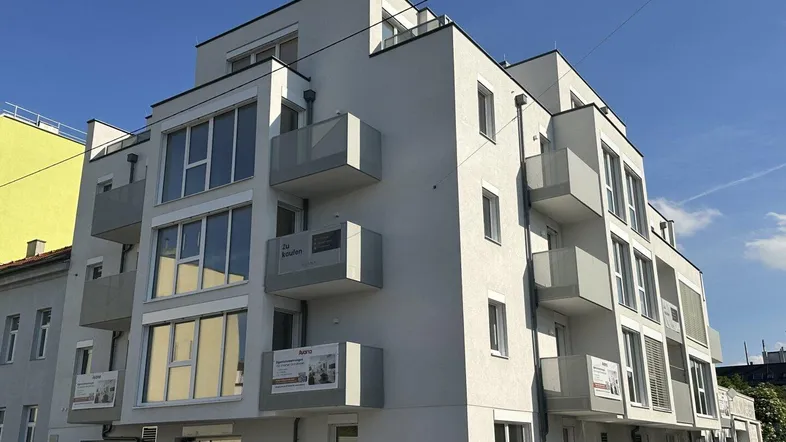 Modernes Mehrfamilienhaus mit mehreren Balkonen und zeitgenössischer Architektur unter blauem Himmel.