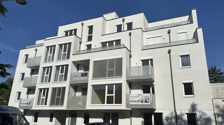 Moderne Wohnanlage mit mehreren Balkonen und großen Fenstern unter blauem Himmel.