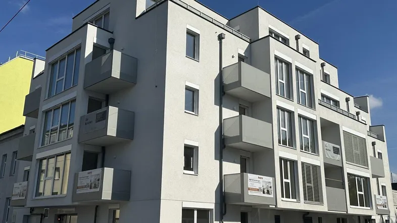 Modernes Mehrfamilienhaus mit Balkonen und großen Fenstern unter blauem Himmel.