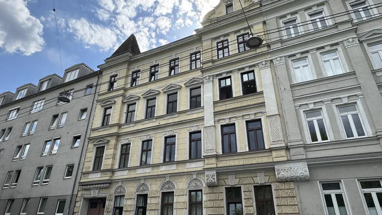 Historische Fassade eines Mehrfamilienhauses mit vielen Fenstern und architektonischen Details unter blauem Himmel.