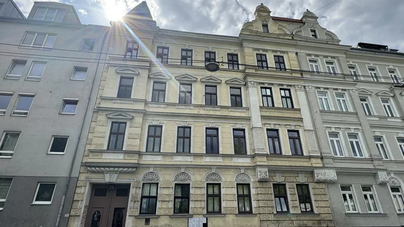 Altes Mehrfamilienhaus mit klassischer Fassade und vielen Fenstern unter bewölktem Himmel.