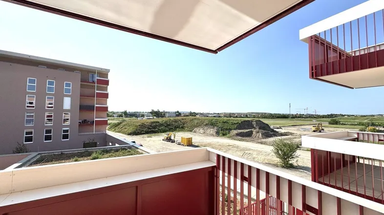 Geräumiger Balkon mit Fliesenboden und Blick auf eine Baustelle sowie weite Felder.