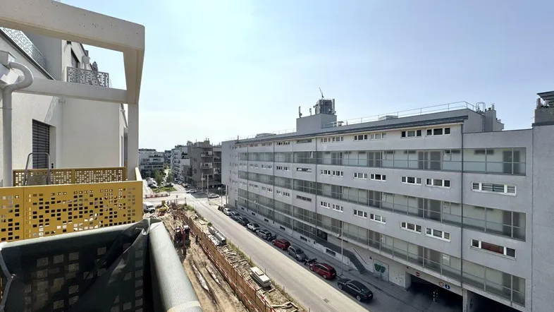 Blick von einem Balkon auf eine städtische Straße mit angrenzenden Gebäuden und einer Baustelle.