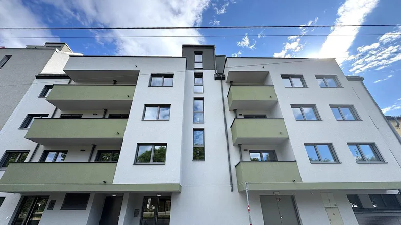 Moderne Wohnhausfassade mit weißen und grünen Akzenten sowie Balkonen unter blauem Himmel.