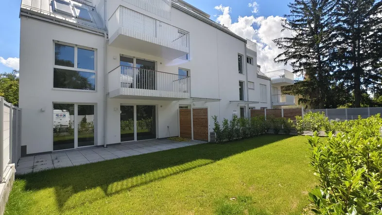 Moderne Wohnanlage mit weißer Fassade, Balkonen und einer gepflegten Rasenfläche im Vordergrund.