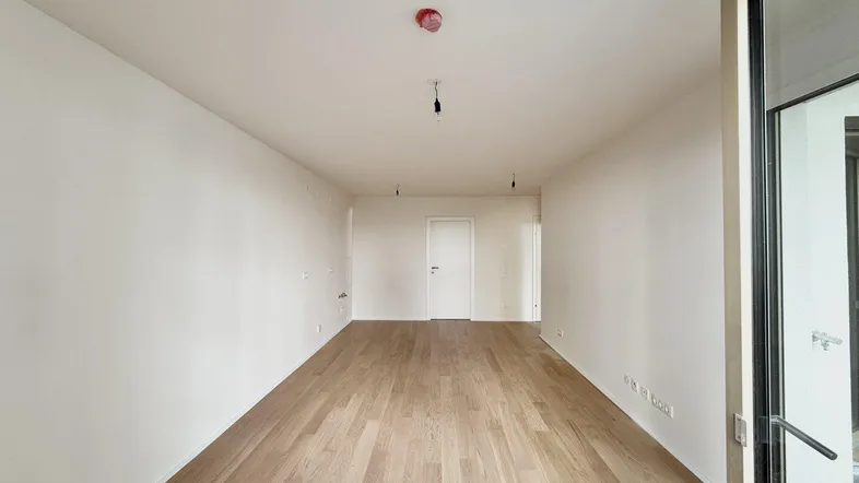 Helles, leeres Wohnzimmer mit Parkettboden und Zugang zu einem Außenbereich.