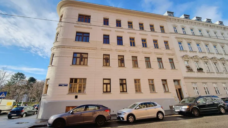 Eckgebäude mit klassischer Architektur und mehreren Stockwerken an einer belebten Straße.