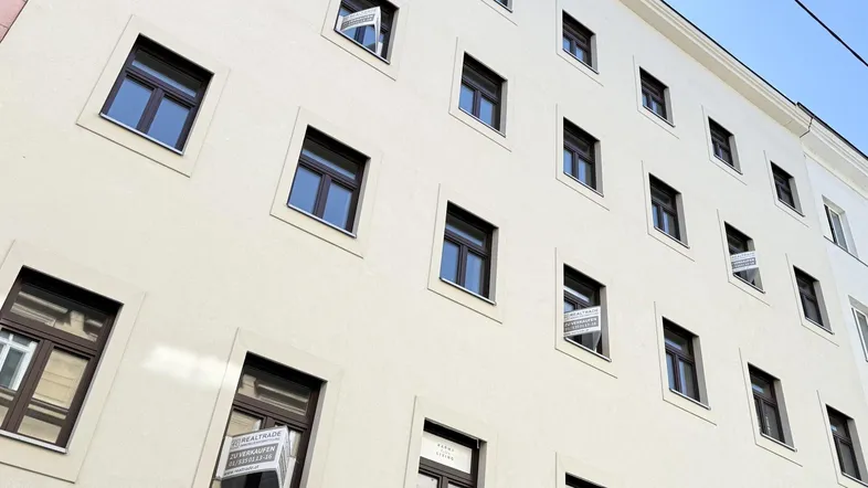 Fassade eines Mehrfamilienhauses mit zahlreichen Fenstern und Verkaufsanzeigen.