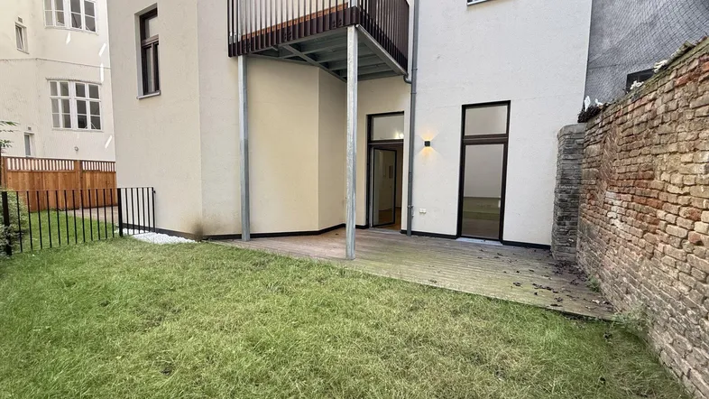 Hinterhof mit kleiner Rasenfläche, Holzterrasse und Zugang zu den Wohnräumen im Erdgeschoss.