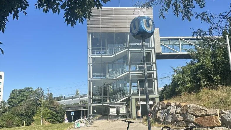 Modernes Gebäude mit Glasfassade und Treppenhaus, umgeben von Grünflächen und Fahrradständern unter blauem Himmel.