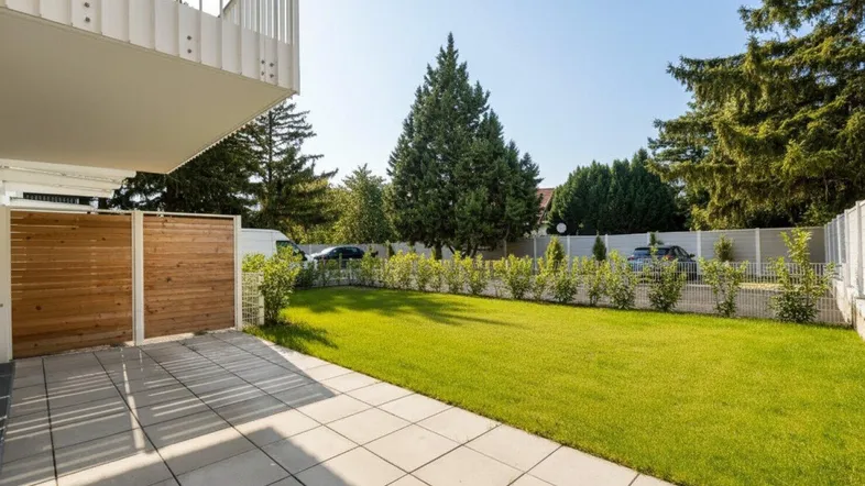 Geräumige Terrasse mit Fliesenboden und angrenzendem gepflegten Rasenbereich unter blauem Himmel.