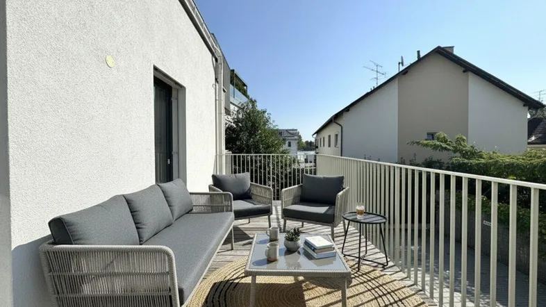 Geräumiger Balkon mit modernen Outdoor-Möbeln und hellem Holzboden unter blauem Himmel.