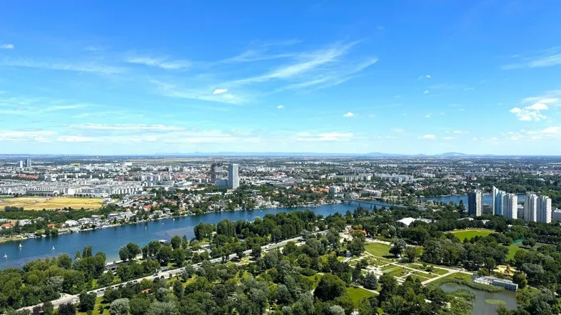 Weitläufige Luftaufnahme der Stadt mit Fluss, Grünflächen und städtischer Bebauung unter blauem Himmel.