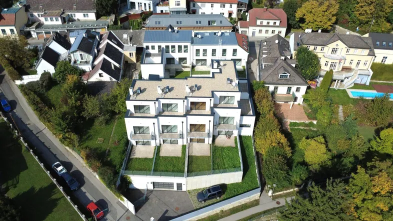 Luftaufnahme eines modernen Wohnkomplexes mit mehreren Einheiten und begrünten Außenbereichen in einer Wohngegend.